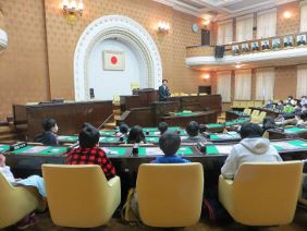 議場で議長の話を聴く生徒の皆さんの写真